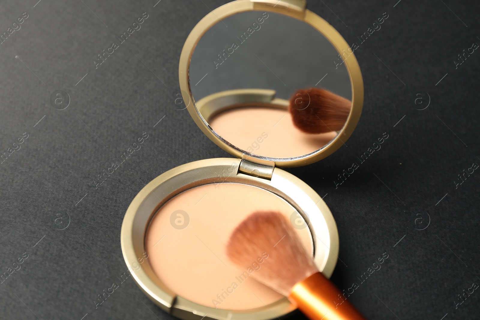 Photo of Open face powder with mirror and brush on black background, closeup