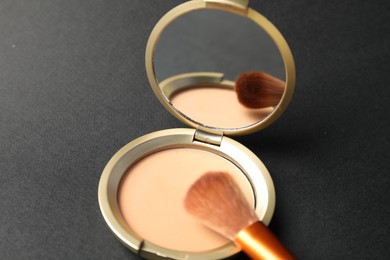 Photo of Open face powder with mirror and brush on black background, closeup