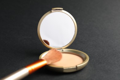 Photo of Open face powder with mirror and brush on black background, closeup