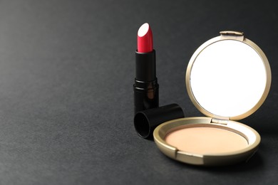 Photo of Open face powder with mirror and lipstick on black background, closeup. Space for text