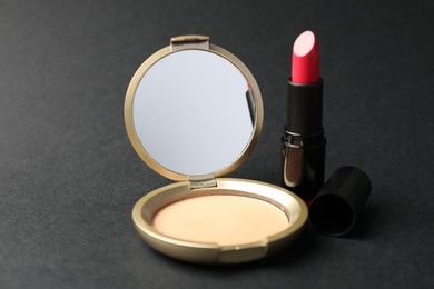 Photo of Open face powder with mirror and lipstick on black background, closeup