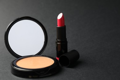 Photo of Open face powder with mirror and lipstick on black background, closeup. Space for text