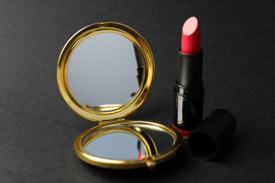 Photo of Open pocket mirror and lipstick on black background, closeup