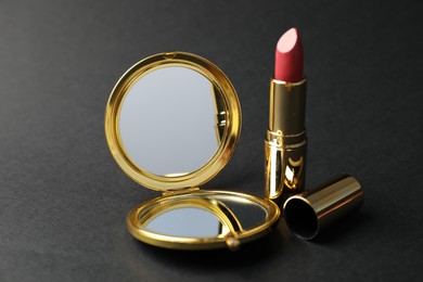 Photo of Open pocket mirror and lipstick on black background, closeup