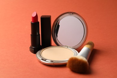 Photo of Open face powder with mirror, lipstick and brush on coral background, closeup