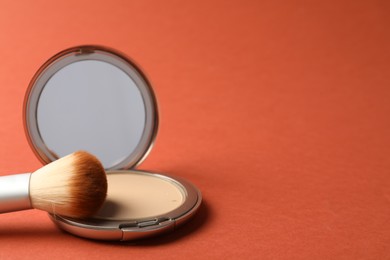 Photo of Open face powder with mirror and brush on coral background, closeup. Space for text