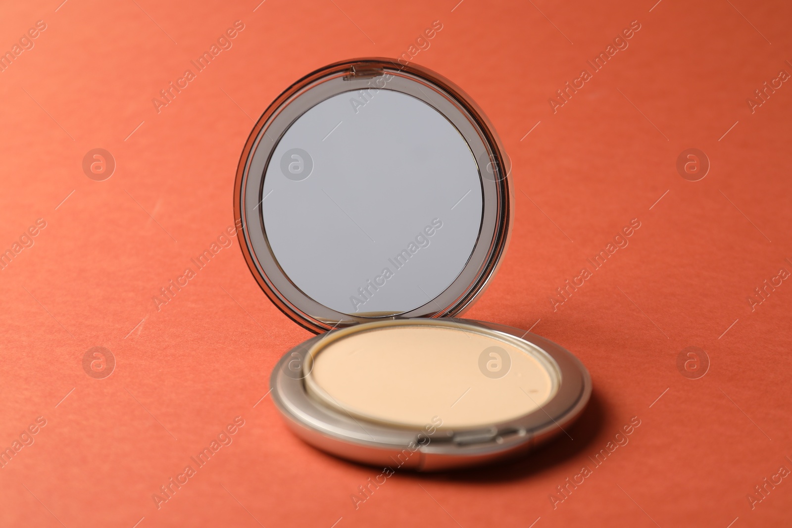 Open face powder with mirror on coral background, closeup Photo of Open face powder with mirror on coral background, closeup