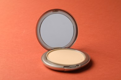 Photo of Open face powder with mirror on coral background, closeup