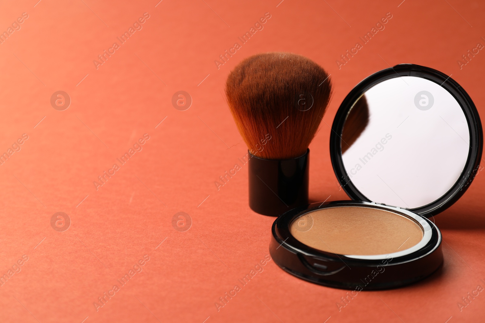 Open face powder with mirror and brush on coral background, closeup. Space for text Photo of Open face powder with mirror and brush on coral background, closeup. Space for text