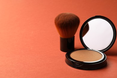 Photo of Open face powder with mirror and brush on coral background, closeup. Space for text