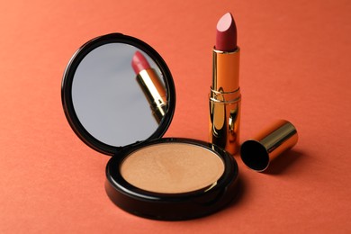 Photo of Open face powder with mirror and lipstick on coral background, closeup