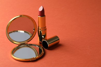 Photo of Open pocket mirror and lipstick on coral background, closeup. Space for text