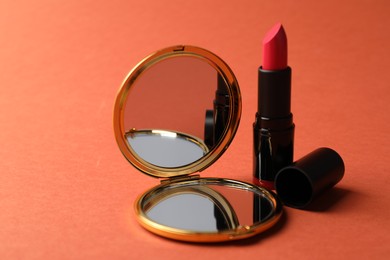 Photo of Open pocket mirror and lipstick on coral background, closeup
