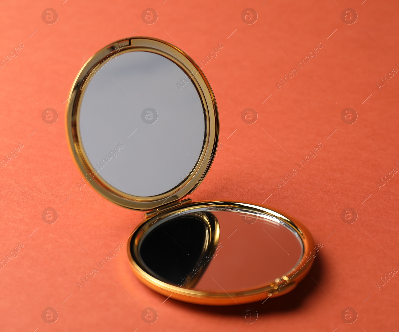 Photo of Open pocket mirror on coral background, closeup