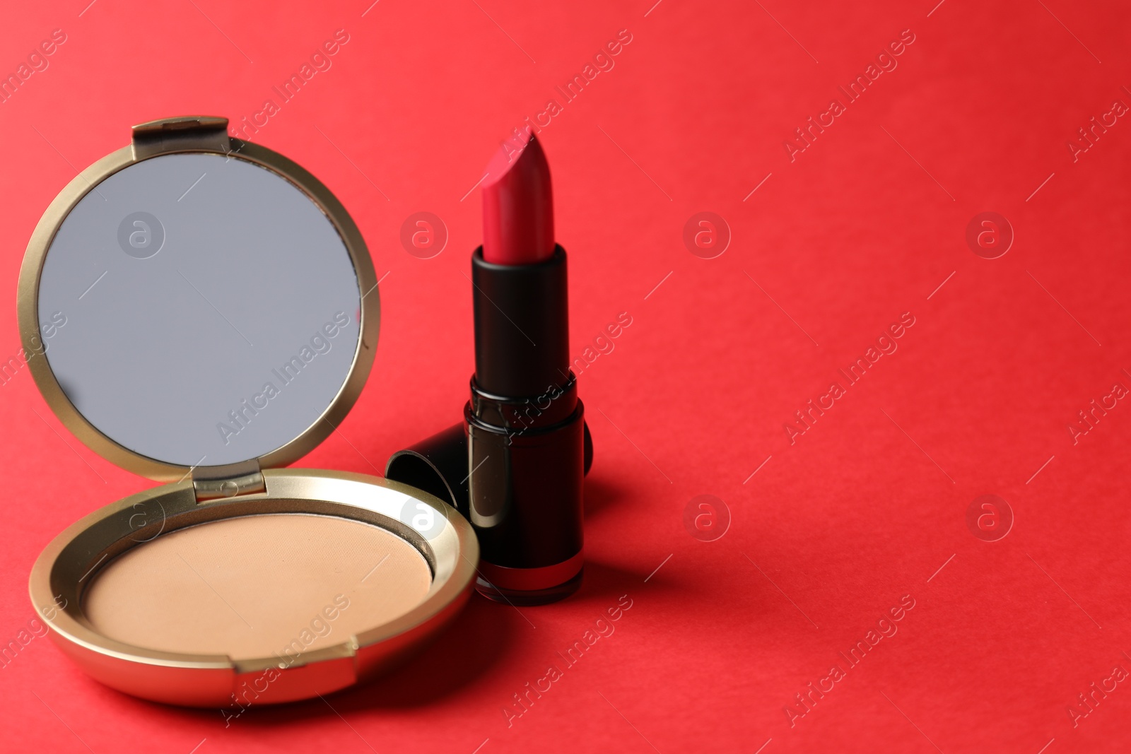 Open face powder with mirror and lipstick on red background, closeup. Space for text Photo of Open face powder with mirror and lipstick on red background, closeup. Space for text