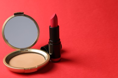 Photo of Open face powder with mirror and lipstick on red background, closeup. Space for text
