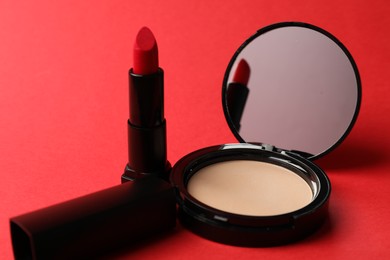 Photo of Open face powder with mirror and lipstick on red background, closeup