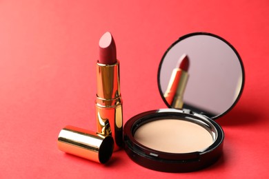 Photo of Open face powder with mirror and lipstick on red background, closeup