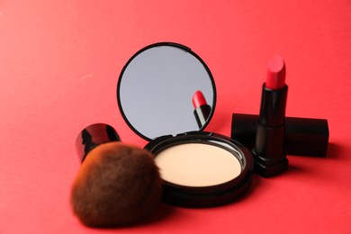 Photo of Open face powder with mirror, lipstick and brush on red background, closeup