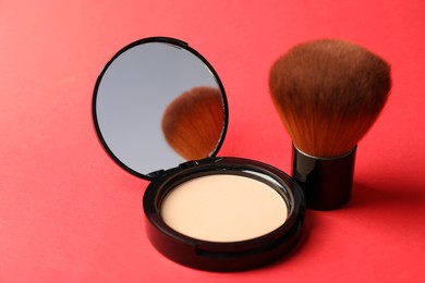 Photo of Open face powder with mirror and brush on red background, closeup