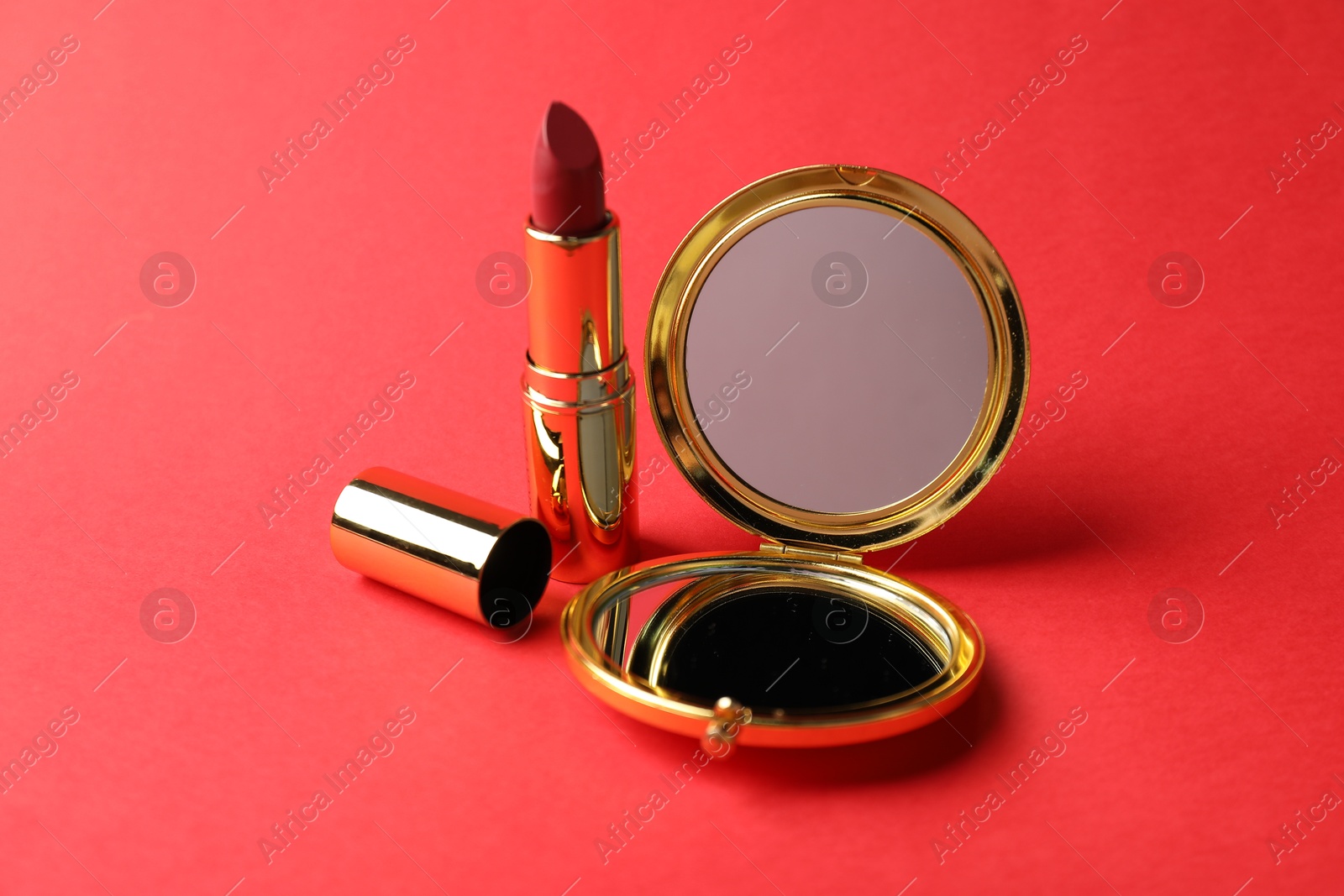 Open pocket mirror and lipstick on red background, closeup Photo of Open pocket mirror and lipstick on red background, closeup