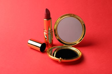 Photo of Open pocket mirror and lipstick on red background, closeup