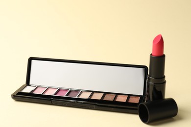 Photo of Eyeshadow palette with mirror and lipstick on beige background, closeup