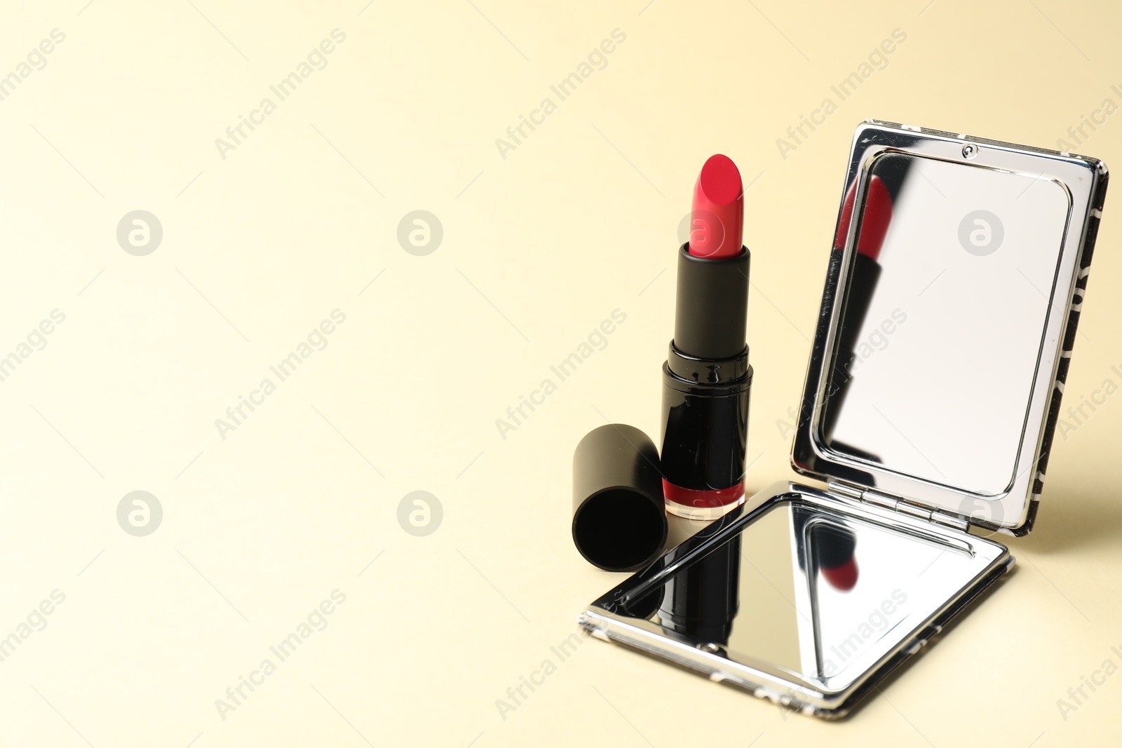 Open pocket mirror and lipstick on beige background, closeup. Space for text Photo of Open pocket mirror and lipstick on beige background, closeup. Space for text