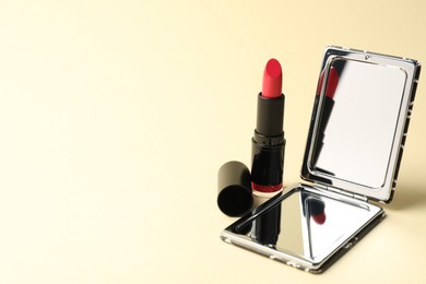 Photo of Open pocket mirror and lipstick on beige background, closeup. Space for text