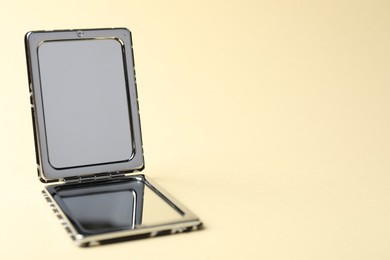 Photo of Open pocket mirror on beige background, closeup. Space for text