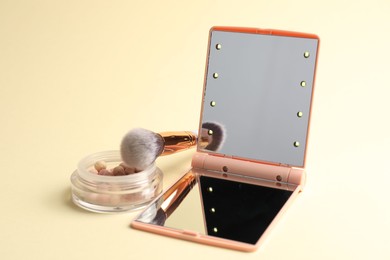 Photo of Open pocket mirror, brush and blush on beige background, closeup