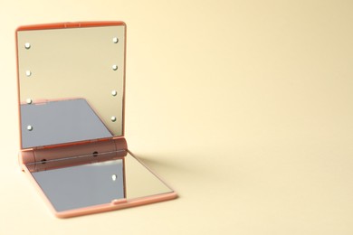 Photo of Open pocket mirror on beige background, closeup. Space for text