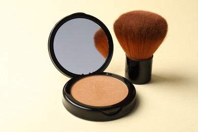 Photo of Open face powder with mirror and brush on beige background, closeup