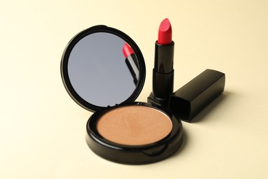 Photo of Open face powder with mirror and lipstick on beige background, closeup