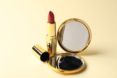 Photo of Open pocket mirror and lipstick on beige background, closeup