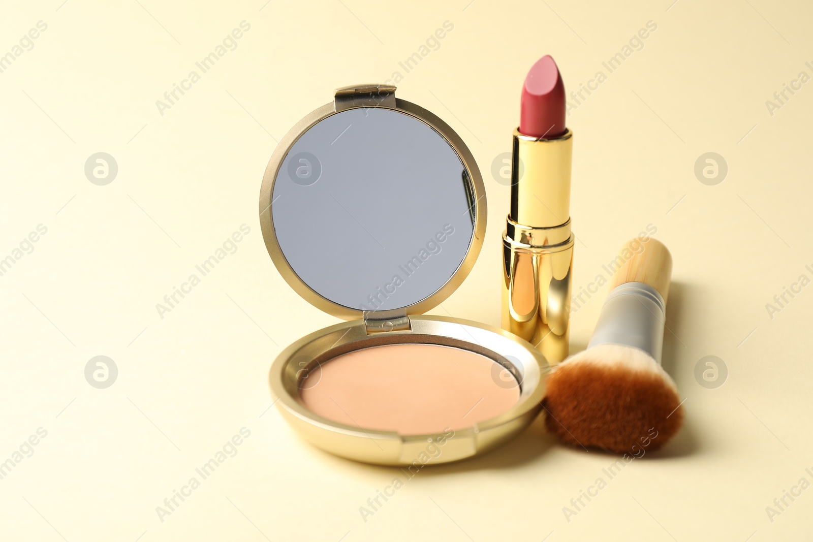 Open face powder with mirror, lipstick and brush on beige background, closeup Photo of Open face powder with mirror, lipstick and brush on beige background, closeup
