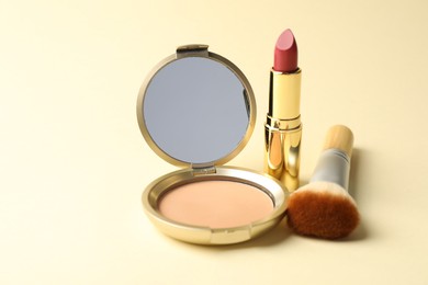 Photo of Open face powder with mirror, lipstick and brush on beige background, closeup