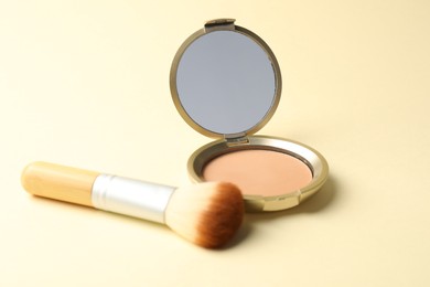 Photo of Open face powder with mirror and brush on beige background, closeup