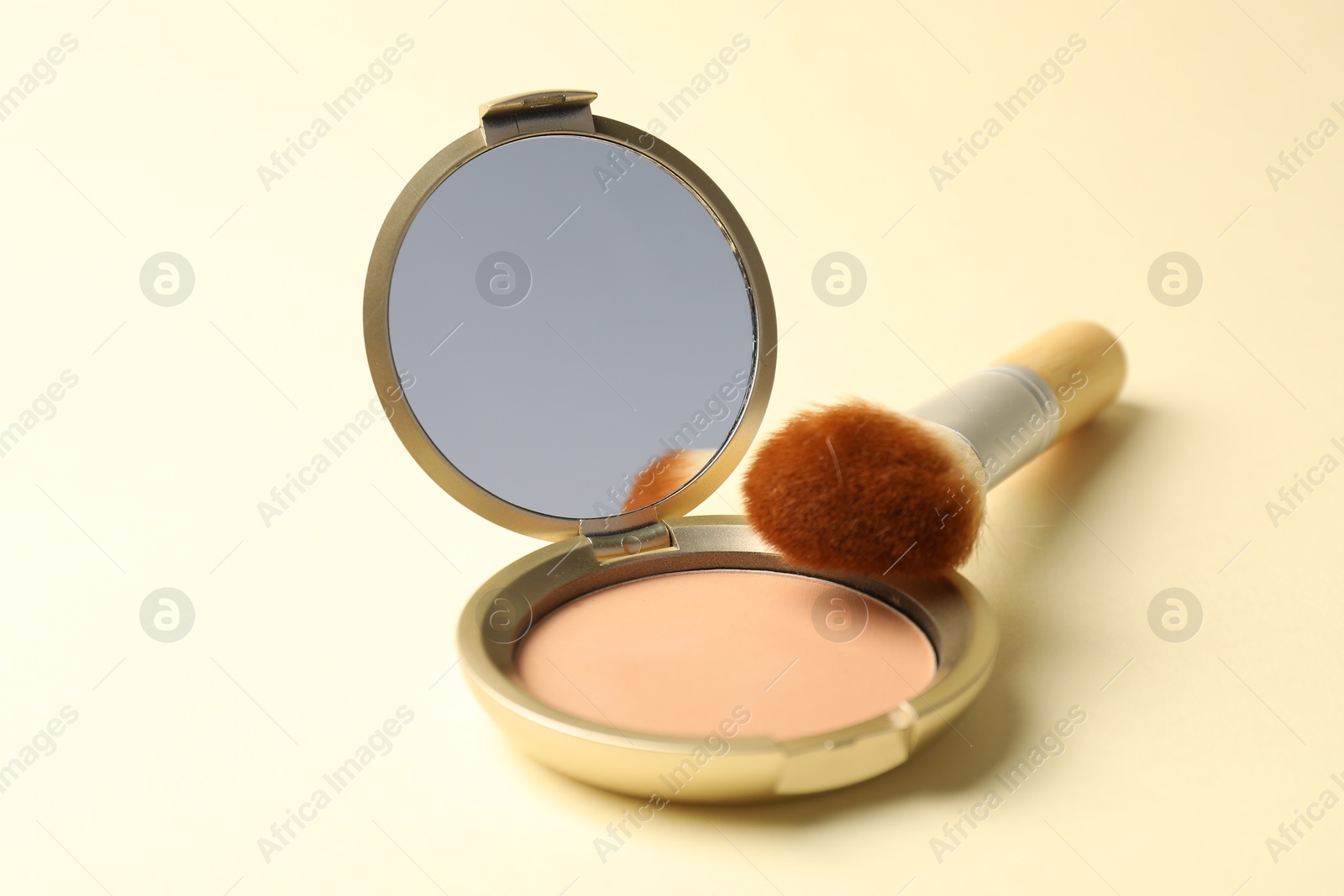 Open face powder with mirror and brush on beige background, closeup Photo of Open face powder with mirror and brush on beige background, closeup