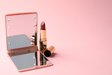 Photo of Open pocket mirror and lipstick on pink background, closeup. Space for text