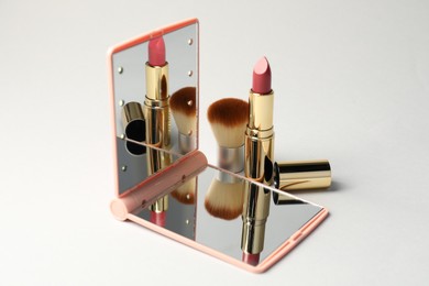 Photo of Open pocket mirror, brush and lipstick on light grey background, closeup