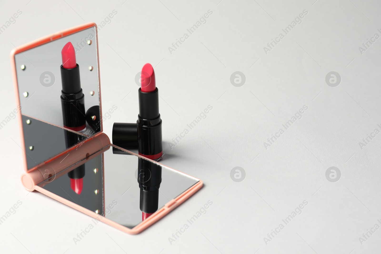Open pocket mirror and lipstick on light grey background, closeup. Space for text Photo of Open pocket mirror and lipstick on light grey background, closeup. Space for text