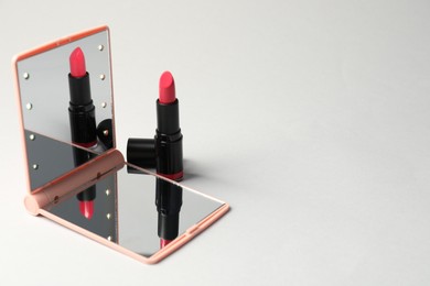 Photo of Open pocket mirror and lipstick on light grey background, closeup. Space for text