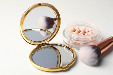 Photo of Open pocket mirror, brush and blush on light grey background, closeup