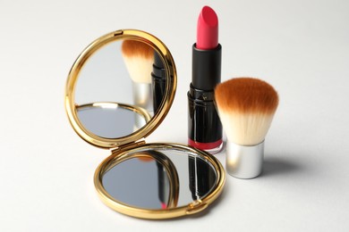 Photo of Open pocket mirror, brush and lipstick on light grey background, closeup