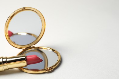 Photo of Open pocket mirror and lipstick on light grey background, closeup. Space for text
