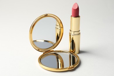 Photo of Open pocket mirror and lipstick on light grey background, closeup