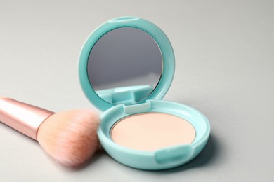 Photo of Open face powder with mirror and brush on light grey background, closeup