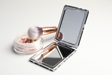 Photo of Open pocket mirror, brush and blush on light grey background, closeup