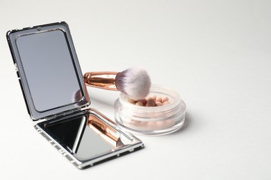 Photo of Open pocket mirror, brush and blush on light grey background, closeup. Space for text